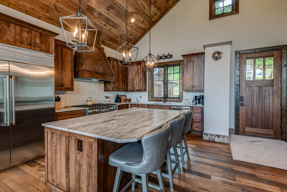 A modern, fully equipped kitchen featuring a large island, stainless steel appliances, wooden cabinetry, and hanging light fixtures. The layout is open and inviting, perfect for cooking and entertaining guests while staying connected to the living and dining spaces.