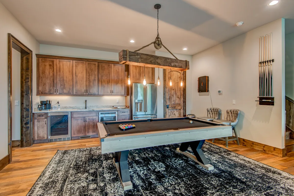A vibrant interior scene focused on a pool table, wood cabinetry, a chandelier, and an area rug. The space is set for lively social gatherings and fun games, embodying the energy of group entertainment.