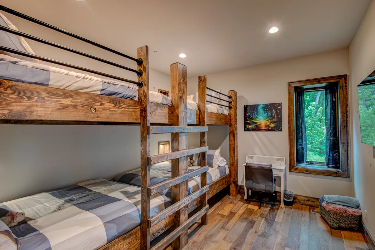 A cheerful and playful bunk room with two sets of queen-over-queen bunk beds, colorful bedding, a large window with a view, and a small desk area for activities or quiet moments. Artwork and playful details make this a haven for younger guests.