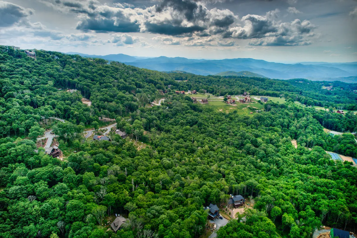 A panoramic mountain view encompassing lush green forests, distant peaks, and scattered houses. The scene promises outdoor adventure, from hiking and ATV explorations to serene moments enjoying the vistas.