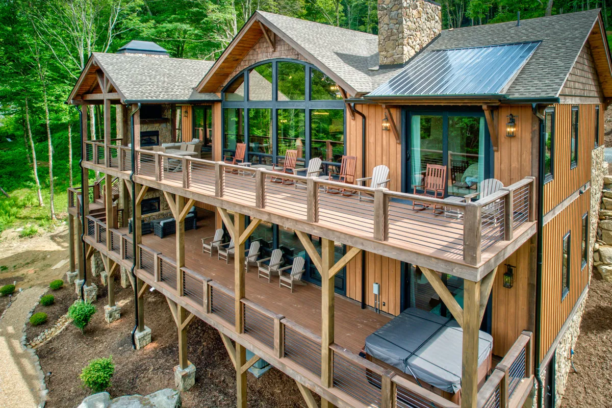 This image highlights a spacious deck with comfortable seating, large windows, a stone chimney, and the lush surrounding greenery. The deck offers ample space for outdoor meetings, breakout sessions, or enjoying a hot tub under the stars.