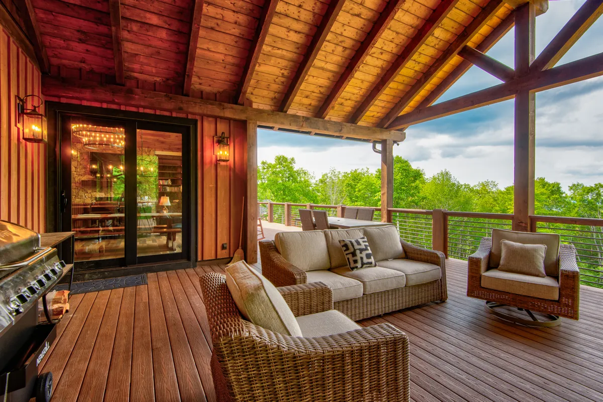 An inviting deck area with cushioned seating, an outdoor grill, and sweeping views of surrounding greenery framed by wooden beams and ceilings. The space is designed for both socializing and peaceful moments in nature, ideal for pet owners and families alike.